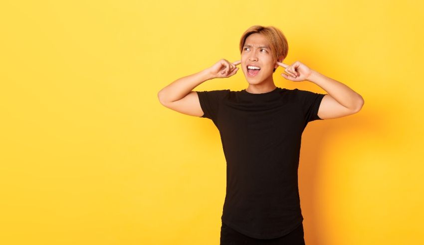 Young asian man covering his ears against a yellow background.